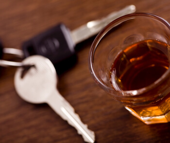 shot glass full of dark colored alcohol on top of a bar table along with a set of car keys. Drinking and driving series. Also driving under the influence of alcohol.